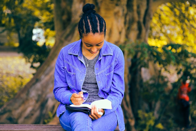 A young woman sitting on a park bench writing in a notebook