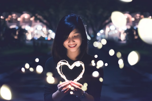 A young woman expressing self-compassion by holding an illuminated heart