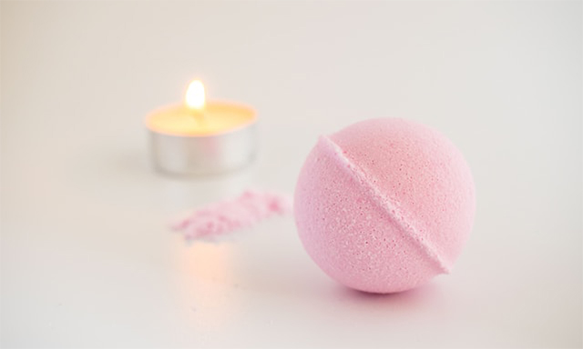 A pink bath bomb alongside a lit candle