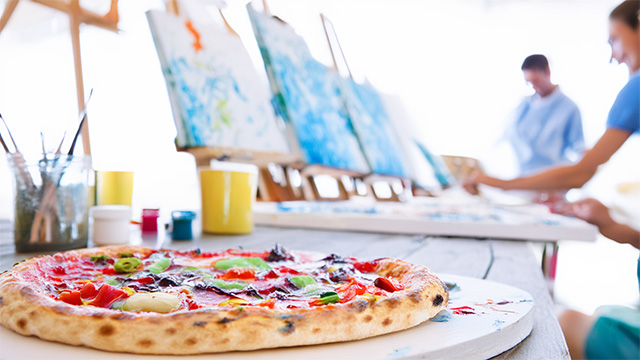 Image of a pizza with people painting on canvas in the background