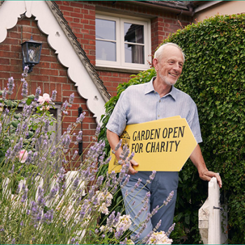 National Garden Scheme banner. Image shows Doug Copeland from Essex carrying a placard that reads Garden Open for Charity.