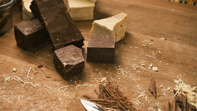 Blocks of different types of chocolate being cut on a chopping board