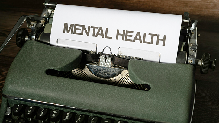 An old style green typewriter. The paper coming out of the roller has the words in bold letters MENTAL HEALTH