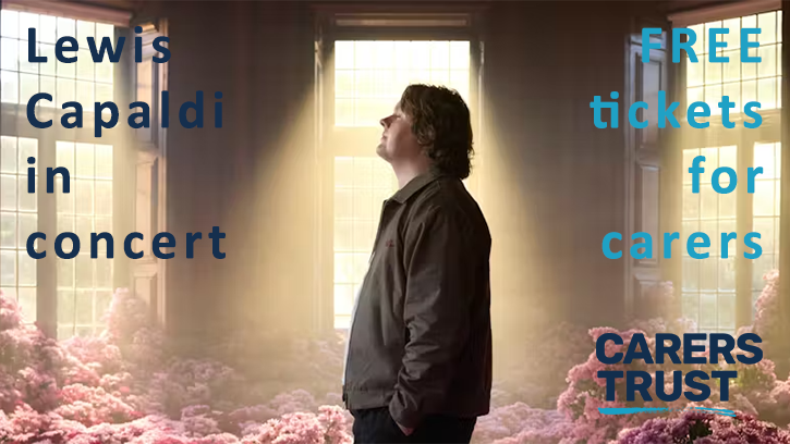 Lewis Capaldi concert for carers banner. Image shows Lewis Capaldi standing in a dimly lit room surrounded by pink flowers