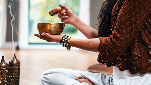 Sound Healing – Time to Reconnect. Woman sitting cross legged on the floor, holding a gong bowl over burning incense.