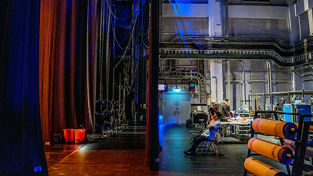 Theatre Tour – Behind the Curtain. Half and half shot of the back stage of a theatre. One side is the stage and the other is the inner workings.