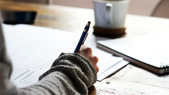 Therapeutic Creative Writing – Words Between Us. Papers and workbooks across the table, coffee in the distance and a woman writing.