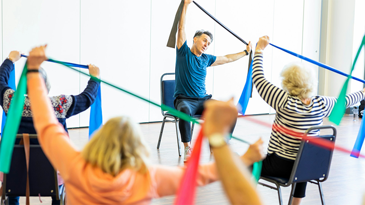 A group of people exercising in chairs with colourful stretch bands over their heads