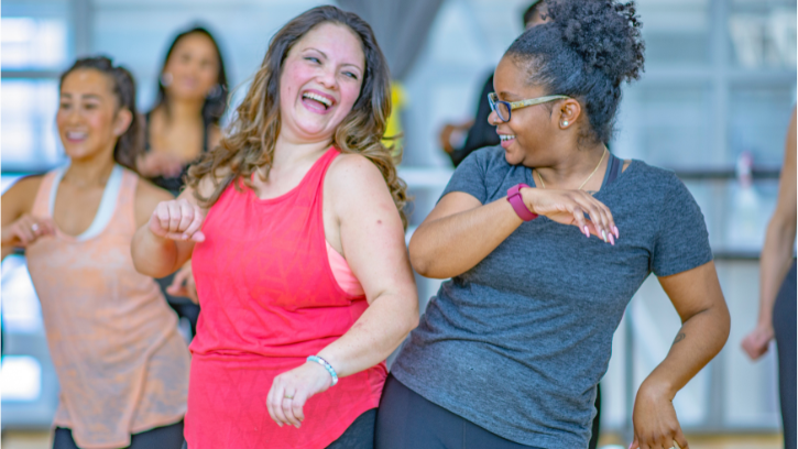 Two carers bump hips and laugh, while participating in a dance class