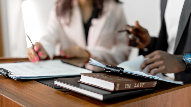 A carer and legal profesisonal sit side by side. Books and flip charts on the table as they discuss LPA and Wills
