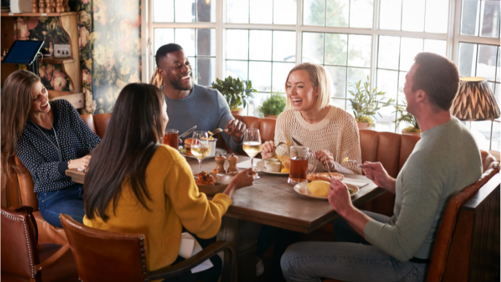 A group of carers sit around a table at a pub, eating, drinking and making conversation