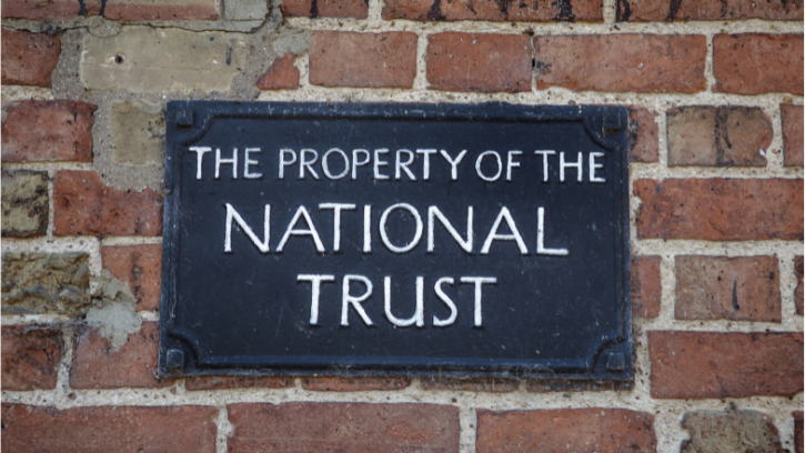An old brinck wall displays a 'The property of the National Trust' metal sign.