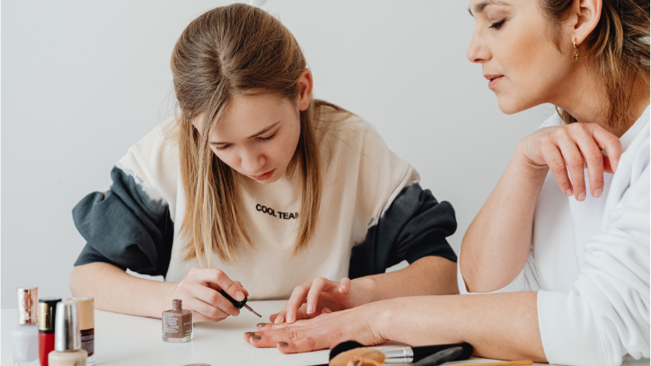 a young carer painting someone's nails with the relevant equipment spread on the table in front of them