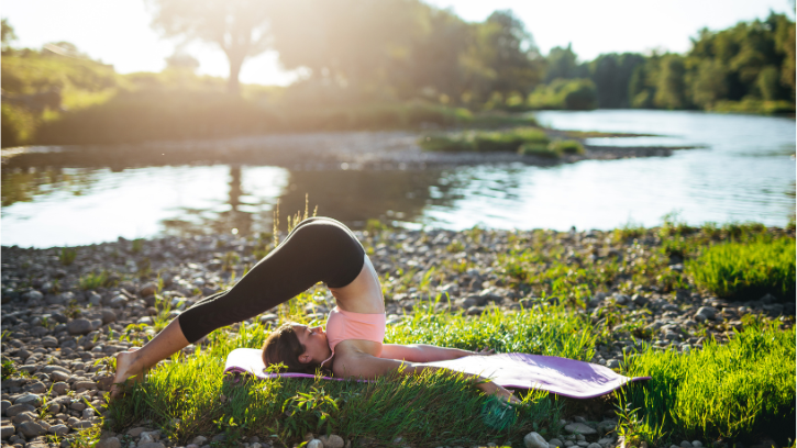 Carer folds backwards on the riverbank, sitting atop a purple yoga mat